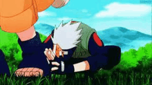 kakashi is laying on his stomach in the grass while naruto is standing next to him .