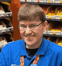 a young man wearing glasses and a blue shirt is smiling in front of a shelf of lego bricks .