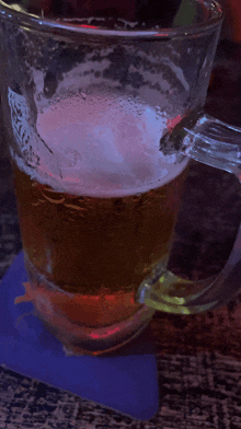 a glass of beer sits on a purple coaster on a wooden table