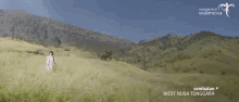 a woman stands in a grassy field with mountains in the background and the words west nusa tenggala on the bottom