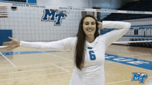 a woman wearing a white shirt with the number 6 on it stands in front of a volleyball net