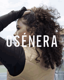 a woman with curly hair is standing in front of a sign that says " osenera "