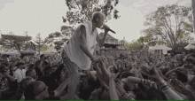 a man singing into a microphone in front of a crowd with the number 177 on a tent in the background