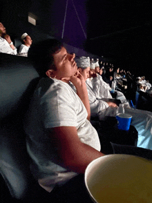 a group of people sitting in a theater watching a movie with a bowl of popcorn in front of them