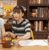 a woman sits at a table with a yellow teddy bear on top of her head