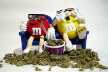 two m & m 's are sitting on a couch eating marijuana .