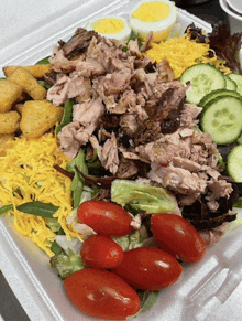 a salad in a styrofoam container with tomatoes nuggets cheese and hard boiled eggs