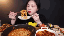 a woman is eating noodles with chopsticks from a bowl while sitting at a table with plates of food .