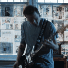 a man playing a guitar in front of a wall with newspapers on it including one that says " division "