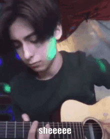 a young man is playing a guitar in a dark room with a green light behind him .