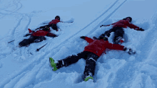 three people are laying in the snow and one of them is wearing a red jacket that says ' salomon ' on the back