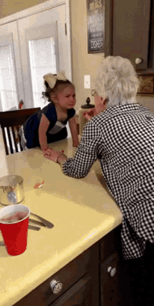 a little girl is sitting at a table with an older woman in a kitchen with a sign that says hugs over dishes