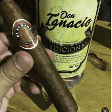 a person is holding a cigar next to a bottle of don ignacio tequila