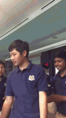 a man wearing a blue shirt with a gold emblem on the front stands in front of a digital clock that reads 9:41