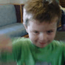 a young boy in a green shirt is sitting on a couch and smiling .