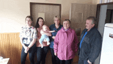 a woman in a pink jacket is holding a baby while three other people stand around her