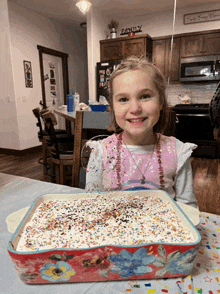 a little girl sitting in front of a cake with sprinkles