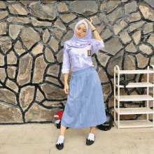 a girl wearing a hijab stands in front of a stone wall next to a shoe rack