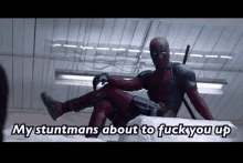 deadpool is sitting on a bed with his legs crossed and says my stuntmans about to fuck you up .