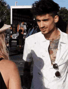 a man with a tattoo on his chest is standing next to a woman in front of a truck .