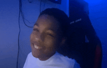 a young boy in a white shirt is smiling in a dark room with a blue light behind him .