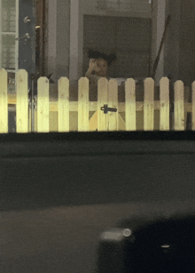 a person behind a white picket fence looking out a window at night