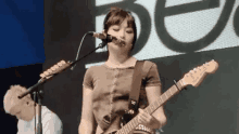 a woman is playing a guitar and singing into a microphone while standing on a stage .