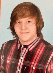 a young man with red hair is wearing a plaid shirt and smiling .