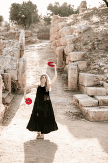 a woman in a black dress is holding two red discs in her hands