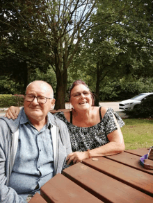 a man and a woman are sitting at a picnic table with trees in the background