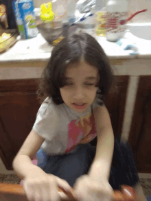 a little girl is sitting in front of a kitchen counter with a box of aquafina water behind her