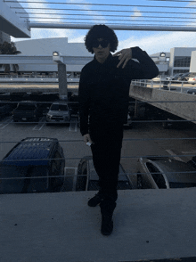 a man wearing sunglasses stands in a parking lot with cars