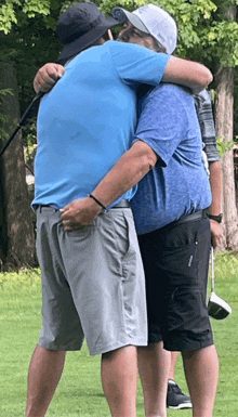 a man in a blue shirt is hugging another man in grey shorts