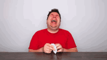 a man in a red shirt is laughing while holding a piece of paper