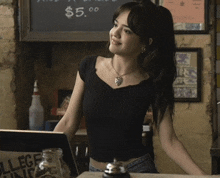 a woman stands behind a counter in front of a chalkboard that says $ 5.00