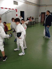 a group of young boys are practicing fencing in a gym with a man standing behind them