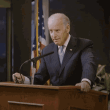 a man in a suit and tie stands in front of a microphone with an american flag in the background