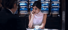 a woman in a white dress is sitting at a table with a cup of coffee .