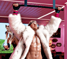 a shirtless man in a fur coat is hanging upside down on a bar