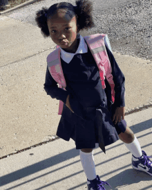 a little girl in a school uniform is standing on the sidewalk