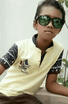 a young boy wearing sunglasses and a yellow shirt with a sailboat embroidered on it