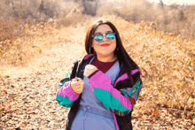 a woman wearing sunglasses and a colorful jacket stands on a dirt path