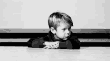 a black and white photo of a young boy sitting at a table with his head resting on his hands .