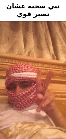 a man wearing a head scarf and a white shirt is giving a peace sign