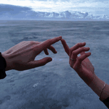 a couple 's hands are reaching out towards each other with a cloudy sky in the background