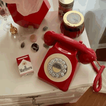 a red telephone and a pack of marlboro cigarettes are on a table .