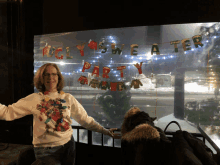 a woman in a sweater stands in front of a sign that says holy sweater