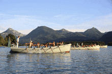 a group of people are rowing boats on a lake with mountains in the background and one of the boats has the word schiffbauer on it