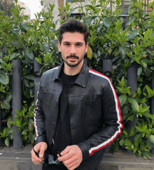 a man wearing a black leather jacket with red and white stripes on the sleeves