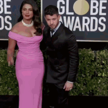 a woman in a pink dress and a man in a black suit are standing on a red carpet at the globe awards .